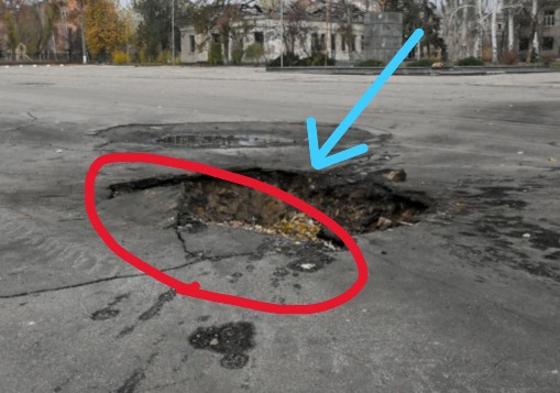 Cropped close-up of the crater showing the uplifted and fractured asphalt edge facing toward the camera.