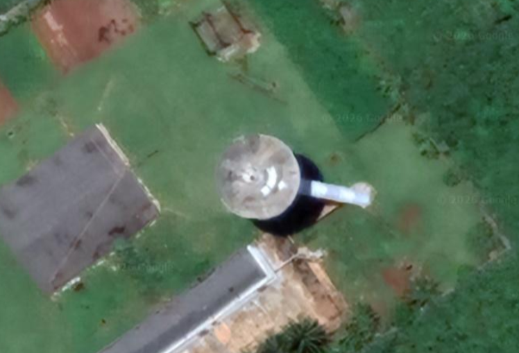 Aerial view of a black-and-white control tower with a circular observation deck, taken from an oblique satellite pass.